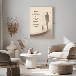May include: A framed artwork with a beige background features two figures and the text: "Behind every overreaction is a younger self begging to be seen and heard." The artwork is displayed in a modern living room setting.