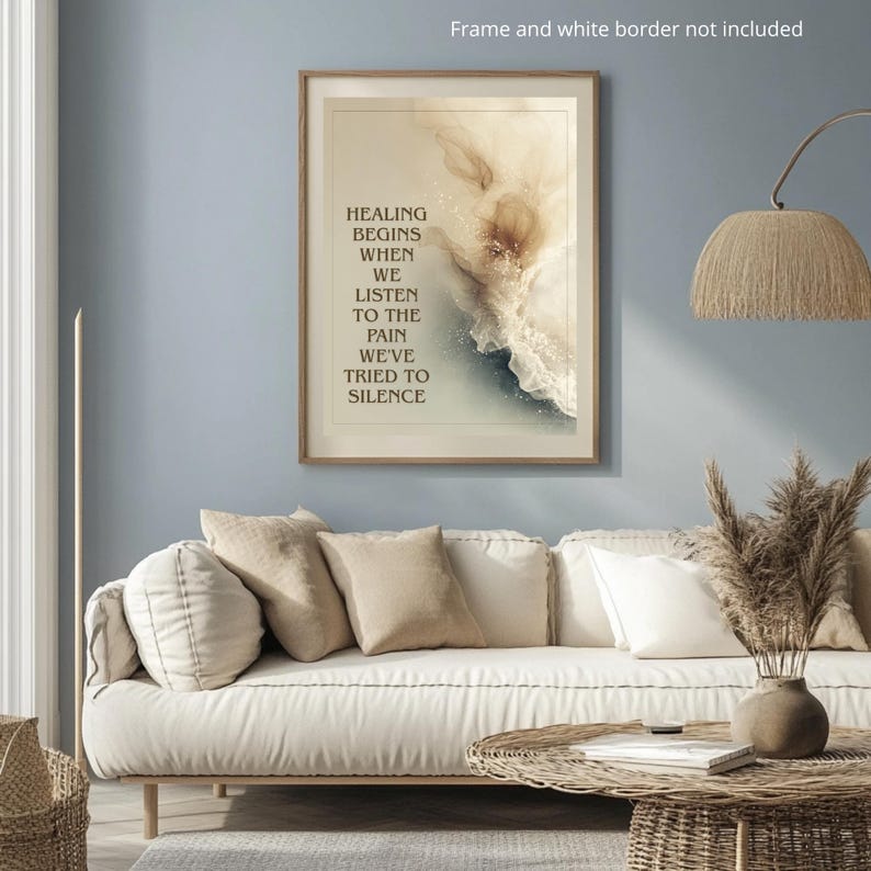 May include: A framed art print with the text "HEALING BEGINS WHEN WE LISTEN TO THE PAIN WE'VE TRIED TO SILENCE." The artwork features an abstract design in beige, white, and blue tones. The print is displayed above a white sofa with beige pillows.