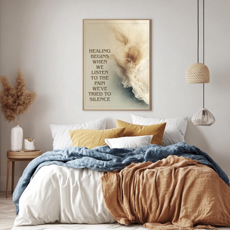 May include: A framed art print with the text "HEALING BEGINS WHEN WE LISTEN TO THE PAIN WE'VE TRIED TO SILENCE" hangs above a bed with white, blue, and orange bedding. The artwork features abstract watercolor-style art in beige and blue tones.
