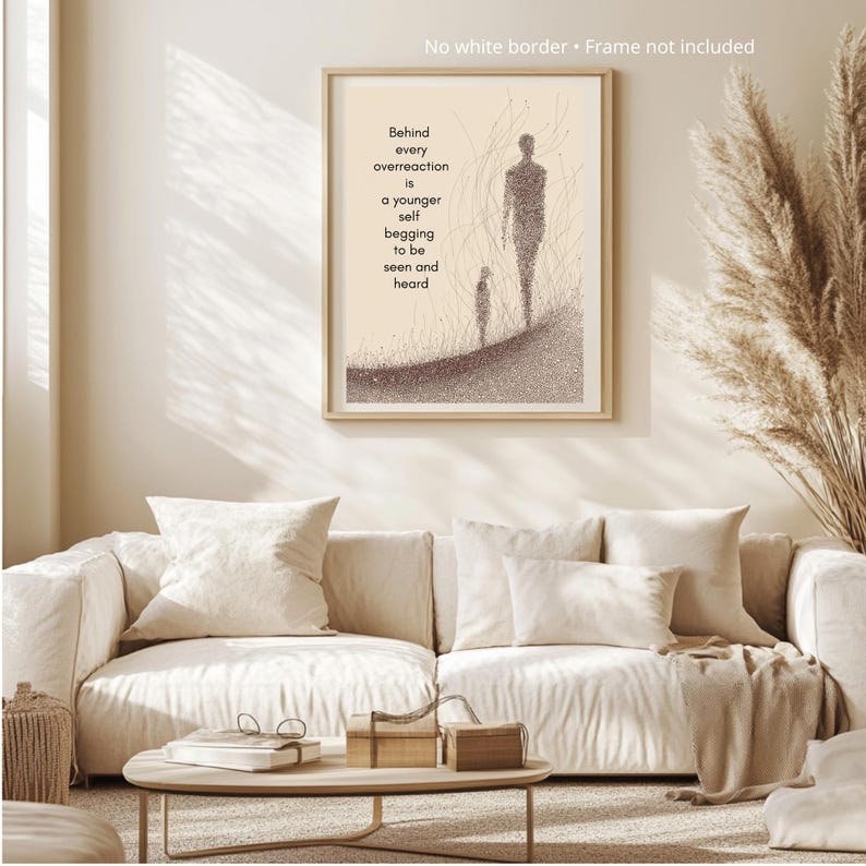 May include: A framed art print with a beige background and a minimalist illustration of two figures. The text reads, "Behind every overreaction is a younger self begging to be seen and heard." The artwork is displayed above a cream-colored sofa.