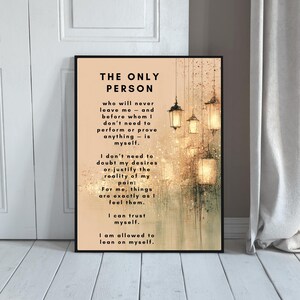 May include: Framed art print with the text "THE ONLY PERSON" in a black frame. The print features inspirational text on a beige background with a blurred, artistic background of hanging lanterns and light.