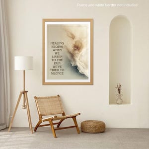May include: A framed print with the text "HEALING BEGINS WHEN WE LISTEN TO THE PAIN WE'VE TRIED TO SILENCE." The artwork features abstract beige and blue tones. A wooden chair, floor lamp, and woven ottoman are in the room.