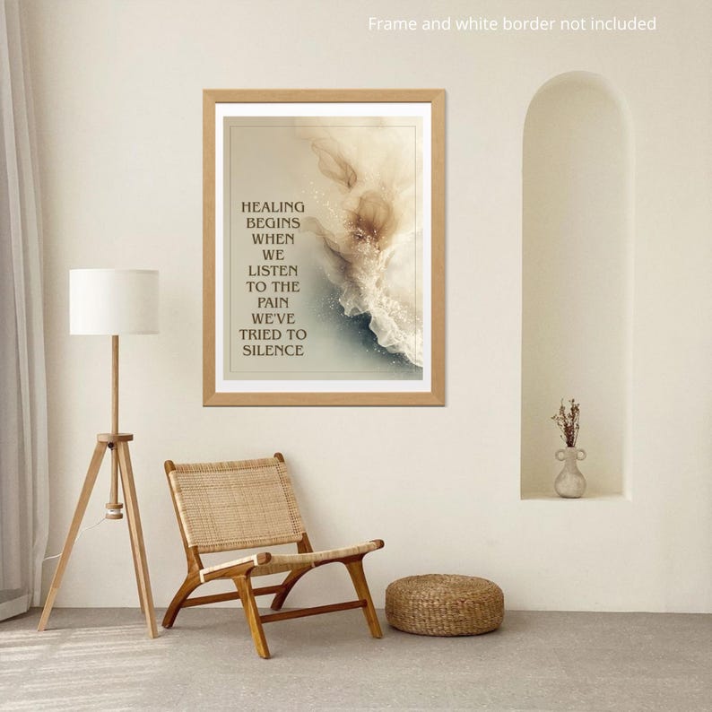 May include: A framed print with the text "HEALING BEGINS WHEN WE LISTEN TO THE PAIN WE'VE TRIED TO SILENCE." The artwork features abstract beige and blue tones. A wooden chair, floor lamp, and woven ottoman are in the room.