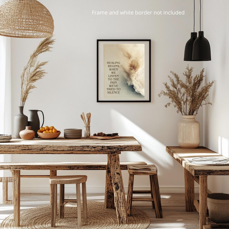 May include: A framed art print with the text "HEALING BEGINS WHEN WE LISTEN TO THE PAIN WE'VE TRIED TO SILENCE" hangs on a white wall. The room features a wooden table, stools, and a bench, with decorative vases and dried plants.