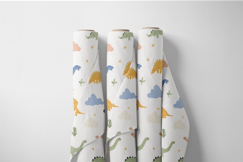 May include: Three rolls of white fabric with a repeating pattern of colorful dinosaurs, clouds, and stars. The dinosaurs are in shades of green, yellow, and blue. The clouds are peach and blue. The fabric is unrolled slightly.