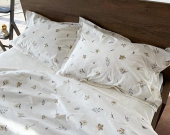 May include: A white bedding set featuring a repeating pattern of small, muted brown flowers and grey leaves. The set includes two rectangular pillowcases and a matching duvet cover, all decorated with the same delicate botanical print.