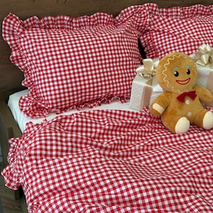 Puede incluir: Juego de cama de cuadros rojos y blancos con bordes con volantes. El juego incluye fundas de almohada y una funda nórdica. Un hombre de jengibre de peluche con pajarita roja está en la cama.