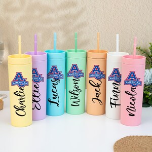 May include: A set of pastel-coloured tumblers with straws, each inscribed with a name in a cursive font. The tumblers are in shades of yellow, lilac, turquoise, mint green, peach, white, and pink, with the "American" logo.