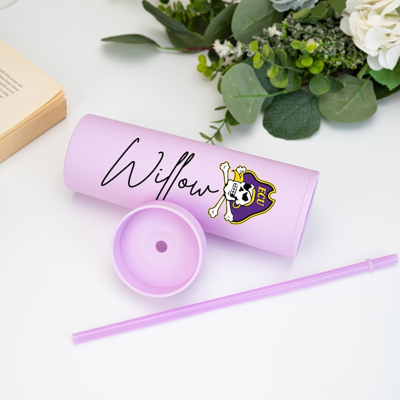 May include: A lilac tumbler with the name "Willow" in cursive. It has an ECU Pirates logo in purple and gold, plus a matching straw. The lid is removed, showing the inside of the tumbler.
