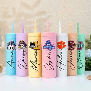 May include: A selection of pastel-coloured tumblers with straws, each personalised with a name in cursive script and a logo. The tumblers are designed for cold drinks. Each tumbler is a different colour, including blue, pink, and yellow.