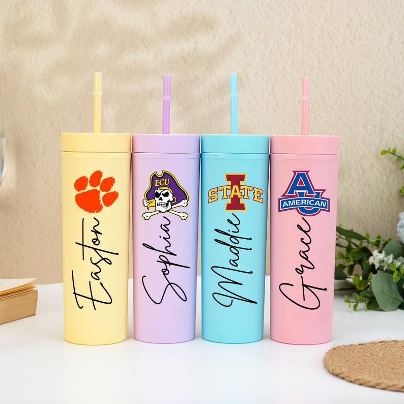 May include: Four pastel-coloured tumblers with lids and straws. Each tumbler is a different colour: yellow, lavender, light blue, and pink. Each has a different design and name printed on it.