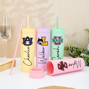 May include: A selection of pastel-coloured tumblers, each with a straw and a unique design. The tumblers feature names and university logos, including Auburn, Washington, and Boston College. One pink tumbler is open, revealing its interior.