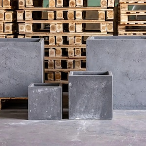 May include: Four grey square planters of different sizes. The planters have a textured surface and a modern, minimalist design. The planters are made of a concrete-like material and are suitable for outdoor or indoor use.
