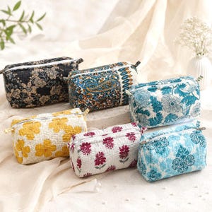 May include: A collection of six rectangular quilted pouches with zippered closures, featuring various patterns including black floral, blue paisley, teal botanical, yellow floral, white with pink floral motifs, and light blue damask prints.