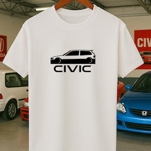 May include: White t-shirt with a black car graphic and the word "CIVIC" underneath. The car graphic is a side profile of a hatchback. The shirt is displayed on a wooden hanger.