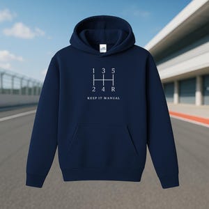 Può includere: Felpa con cappuccio blu navy con tasca frontale. La grafica bianca sul davanti raffigura lo schema del cambio di un'auto con la scritta "1 3 5 2 4 R KEEP IT MANUAL".
