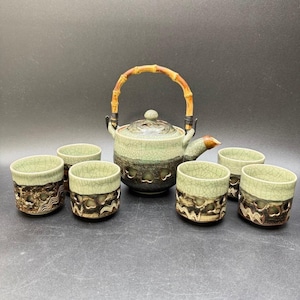 May include: A ceramic tea set featuring a teapot with a bamboo handle and six matching cups. The teapot and cups have a green and brown crackle glaze. The cups have a decorative cut-out design.