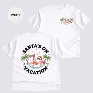 Op de afbeelding: Witte t-shirts met een afbeelding van de Kerstman op vakantie, met een zonnebril en een rode hoed, drijvend op een eenhoorn-zwemband. De tekst "SANTA'S ON VACATION" staat op de achterkant van het shirt.