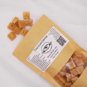 May include: A package of OraFlora Mints with Rich Ginger, and a pile of loose mints. The package is tan with the text "TranscenDental" and "Whole Mouth Care." The mints are small, square, and light brown.