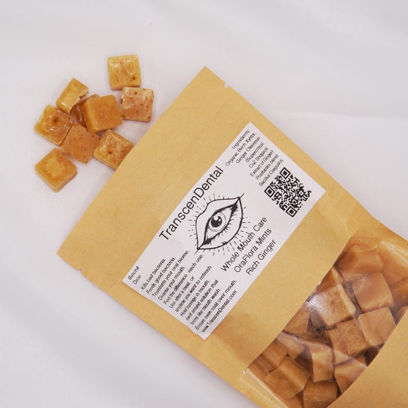 May include: A package of OraFlora Mints with Rich Ginger, and a pile of loose mints. The package is tan with the text "TranscenDental" and "Whole Mouth Care." The mints are small, square, and light brown.
