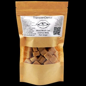 May include: A brown paper bag with a clear window, filled with square, light brown mints. The bag has a label with the text "TranscenDental Whole Mouth Care OraFlora Mints Rich Ginger". The label also lists ingredients and instructions.