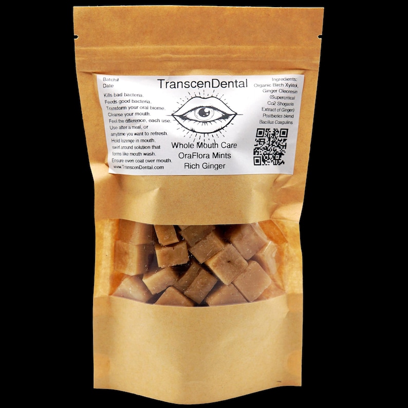 May include: A brown paper bag with a clear window, filled with square, light brown mints. The bag has a label with the text "TranscenDental Whole Mouth Care OraFlora Mints Rich Ginger". The label also lists ingredients and instructions.