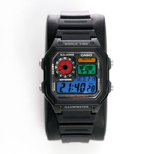 May include: Black Casio digital watch with a rectangular face. The watch displays the time in blue digits, along with a world map and other functions. The watch has the text "WORLD TIME", "CASIO", and "ILLUMINATOR".