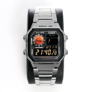 Könnte beinhalten: Eine silberne digitale Casio-Uhr mit einem schwarzen quadratischen Zifferblatt und einem silbernen Armband. Das Zifferblatt zeigt die Uhrzeit, das Datum und andere Funktionen an. Auf der Uhr stehen die Wörter "WORLD TIME", "CASIO" und "ILLUMINATOR".