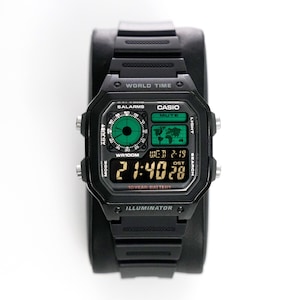 Puede incluir: Un reloj digital Casio negro con una correa de resina negra. La esfera del reloj tiene una pantalla digital que muestra la hora, la fecha y el día de la semana. El reloj también tiene una función de hora mundial, una batería de 10 años y un iluminador.