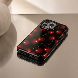 Può includere: Custodia per telefono nera con un motivo di ciliegie rosse. La custodia lucida è progettata per uno smartphone. Le ciliegie, con i loro gambi verdi, sono distribuite uniformemente.
