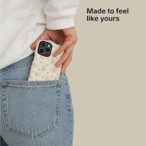 May include: A beige phone case with a repeating pattern of brown teddy bears and bows is partially visible in a back pocket of blue jeans. The phone case is held by a person. The text "Made to feel like yours" is in the upper right corner.