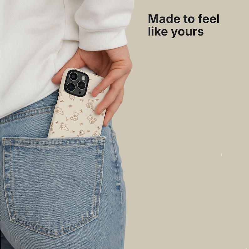 May include: A beige phone case with a repeating pattern of brown teddy bears and bows is partially visible in a back pocket of blue jeans. The phone case is held by a person. The text "Made to feel like yours" is in the upper right corner.
