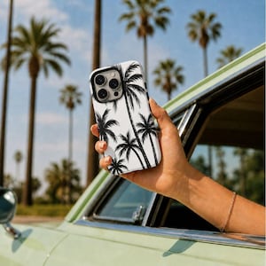 May include: A white phone case featuring a black palm tree design. The case is held up against a backdrop of palm trees and a blue sky. The phone case is a sleek accessory with a tropical theme.