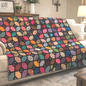 May include: A quilt featuring a repeating pattern of multi-colored octagonal fabric patches in shades of pink, orange, blue, green, and purple, separated by a black lattice grid. The quilt has a gray border and is draped over a beige sofa.