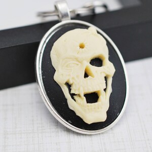 May include: A black and white skull charm with a silver ring. The skull is detailed with a single eye and a toothy grin.