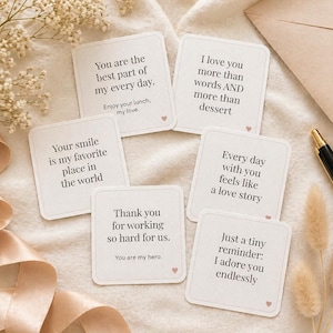 May include: A collection of square cards with romantic quotes in black text, including "You are the best part of my every day" and "I love you more than words." The cards are arranged on a cream-colored surface with a pen and decorative flowers.