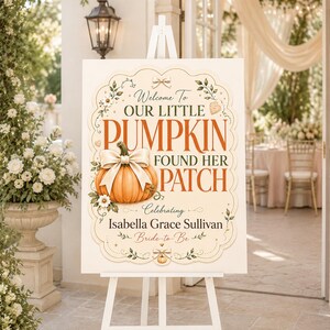 Op de afbeelding: Een wit rechthoekig welkomstbord op een witte ezel met een illustratie van een oranje pompoen met een beige strik, bloemaccenten en de tekst: Welcome To OUR LITTLE PUMPKIN FOUND HER PATCH Celebrating Isabella Grace Sullivan Bride-to-Be.