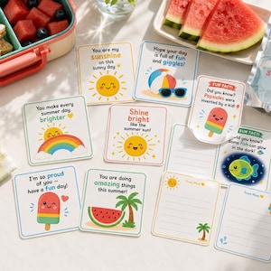 Op de afbeelding: Een verzameling zomerkaarten met vrolijke illustraties en berichten, samen met een lunchbox met sandwiches en watermeloen. Een sapzakje met een zon-afbeelding en zonnebrilvormige zonnebrillen zijn ook aanwezig.