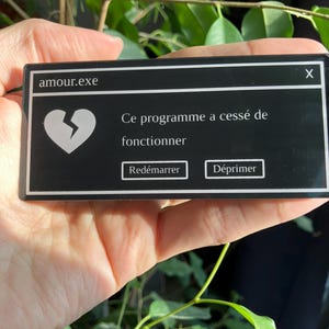 May include: A black rectangular sticker with white text and graphics. The text reads "amour.exe" at the top, with a broken heart graphic. Below, it says "Ce programme a cessé de fonctionner" with "Redémarrer" and "Déprimer" as button options.