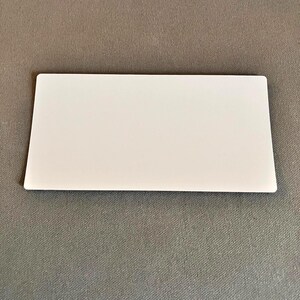 Op de afbeelding: Een wit rechthoekig object met afgeronde hoeken, liggend op een grijze ondergrond. Het object is glad en ondoorzichtig, met een strak, minimalistisch ontwerp. De vorm suggereert een kaart of een vergelijkbaar plat item.