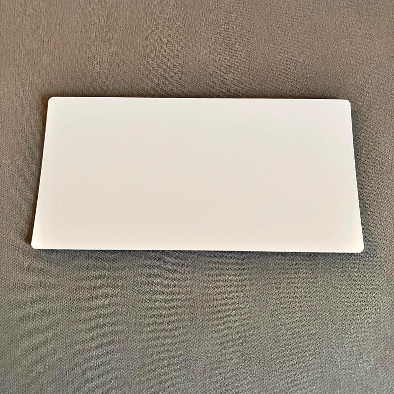 Op de afbeelding: Een wit rechthoekig object met afgeronde hoeken, liggend op een grijze ondergrond. Het object is glad en ondoorzichtig, met een strak, minimalistisch ontwerp. De vorm suggereert een kaart of een vergelijkbaar plat item.