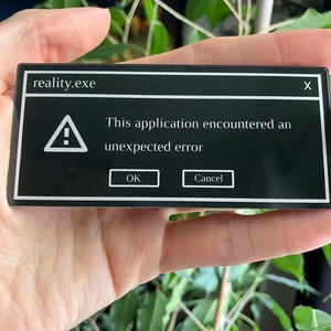 May include: A black rectangular sticker with white text and graphics. The text reads "reality.exe" at the top, and below, "This application encountered an unexpected error." Includes "OK" and "Cancel" buttons.