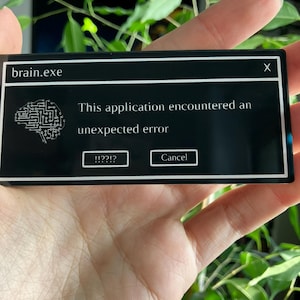 May include: A black rectangular sticker with the text "brain.exe" at the top. The sticker features a graphic of a brain and the message "This application encountered an unexpected error." with "!!??!?" and "Cancel" buttons.