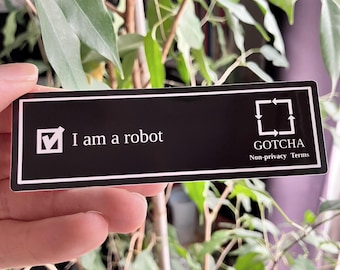 Op de afbeelding: Een zwarte rechthoekige sticker met witte tekst die "I am a robot" en een vinkje weergeeft. De sticker bevat ook de tekst "GOTCHA Non-privacy Terms" en een vierkant met pijlen.