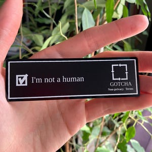 May include: A black rectangular sticker with white text that reads "I'm not a human" and a checkmark in a box. The sticker also has the text "GOTCHA Non-privacy Terms" and a square with arrows.