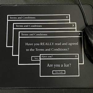 May include: Black mouse mat with a computer pop-up design. The design features white text boxes with the words "Terms and Conditions" and the questions "Have you REALLY read and agreed to the Terms and Conditions?" and "Are you a liar?" A black computer mouse is on the right.