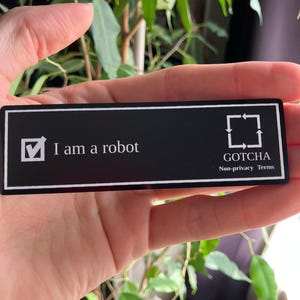 Peut inclure: Une étiquette de nom rectangulaire noire avec le texte blanc "I am a robot" et un symbole de coche. Le coin inférieur droit porte le texte "GOTCHA Non-privacy Terms" et un symbole carré avec des flèches.