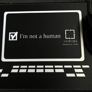 Pode incluir: Tapete de rato retangular preto com um contorno branco de tela de computador e teclado. O texto "I'm not a human" é exibido, juntamente com a palavra "GOTCHA" e "Non-privacy Terms". Um rato de computador preto está à direita.