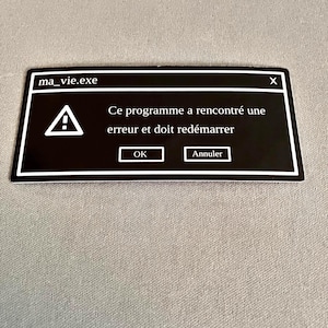 May include: A black sticker with a white border displaying a computer error message. The text reads "ma_vie.exe" at the top, with a warning symbol and the message "Ce programme a rencontré une erreur et doit redémarrer" below. Includes "OK" and "Annuler" buttons.