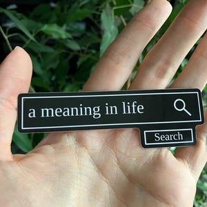 May include: A black rectangular sticker with the text "a meaning in life" in white, resembling a search bar. A magnifying glass icon is on the right. Below, a smaller rectangle reads "Search".